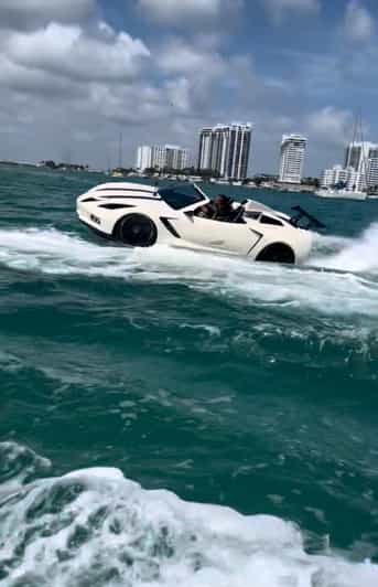 White sports car boat racing across turquoise water with city skyline in the background.
