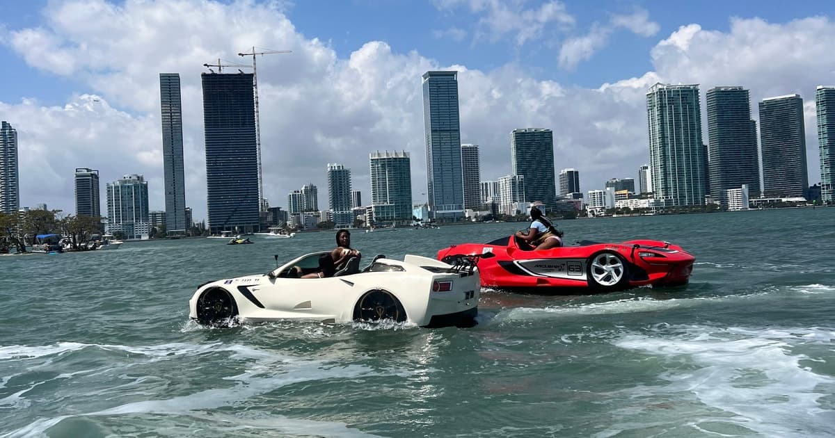 White and red car-shaped boats speed across the water in front of city skyline.