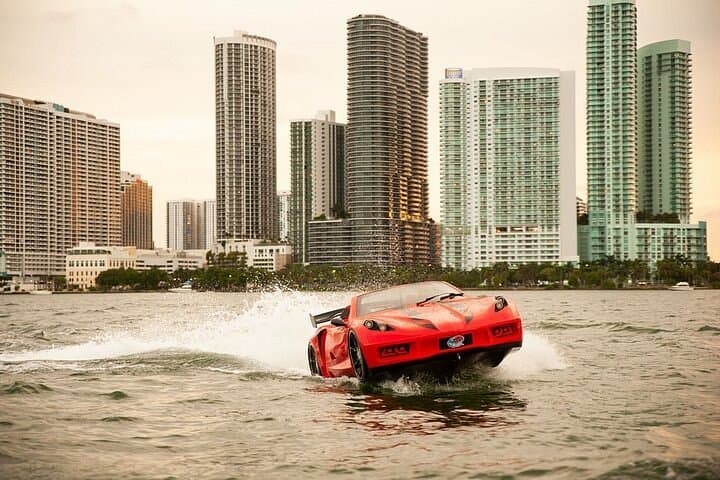 Red sports car-shaped boat speeding across the water in front of a city skyline.